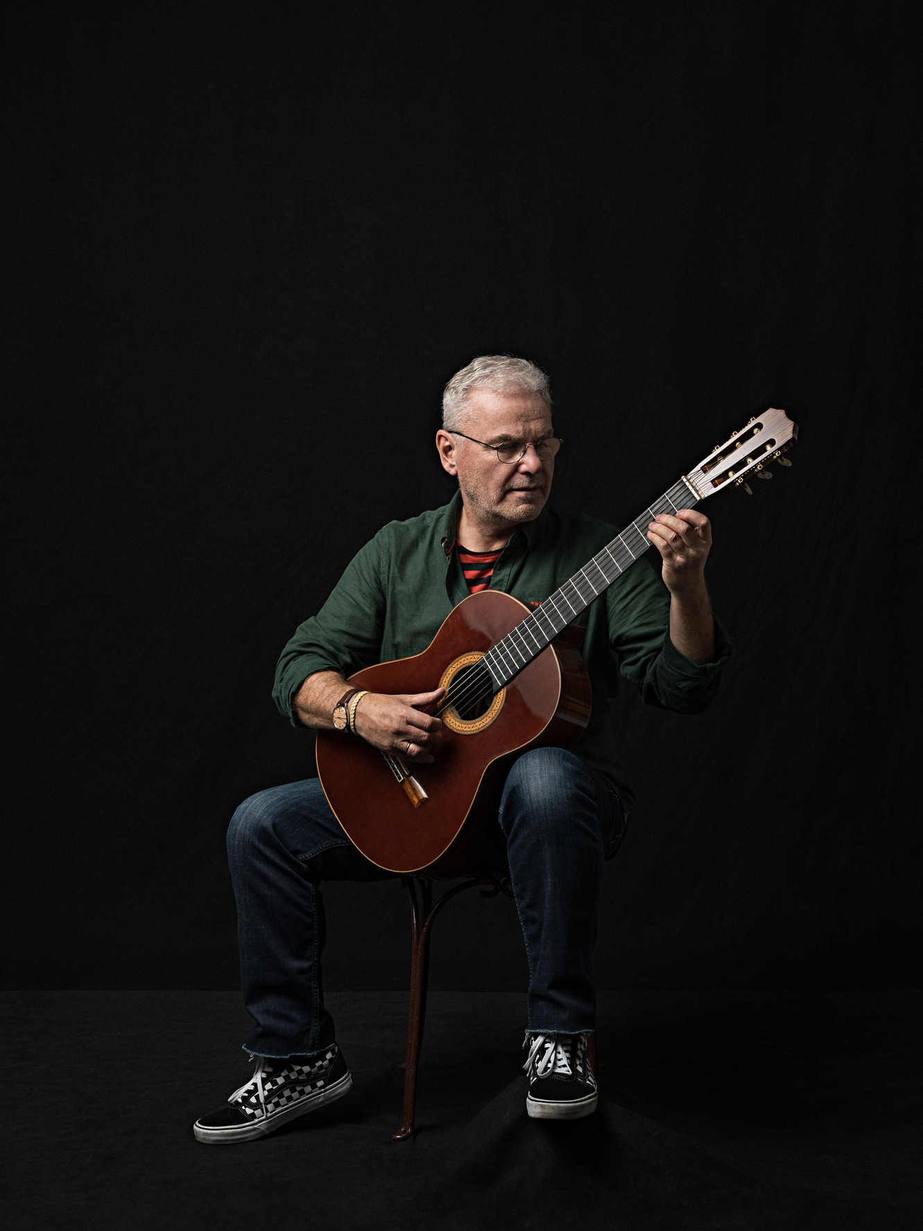 Porträt eines Mannes mit klassischer Gitarre in Spielposition vor schwarzem Studiohintergrund