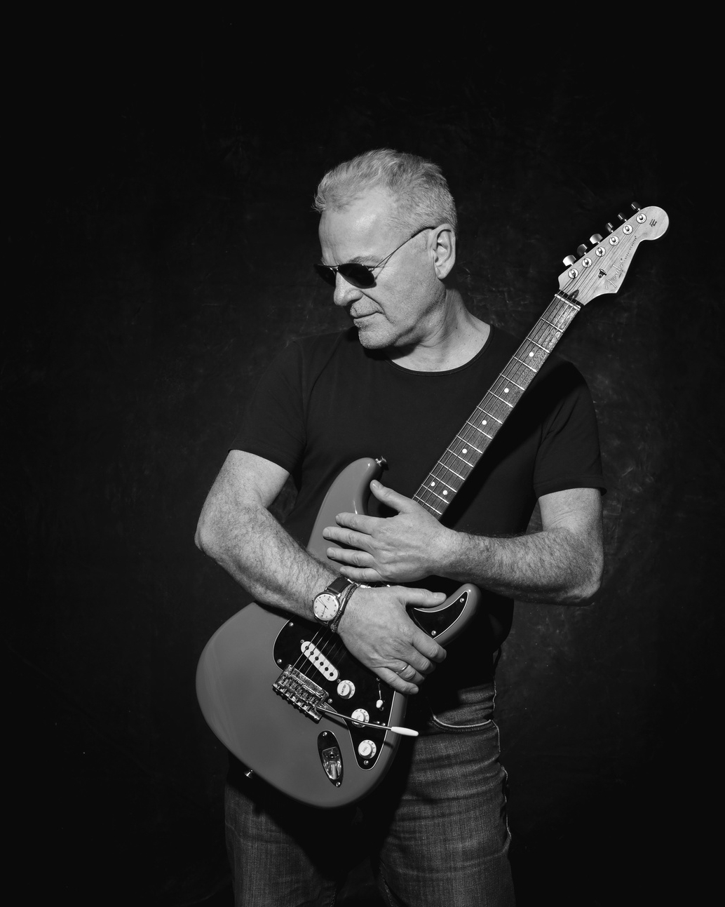 Schwarz-Weiß-Porträt eines Mannes mit E-Gitarre und Sonnenbrille vor schwarzem Studiohintergrund
