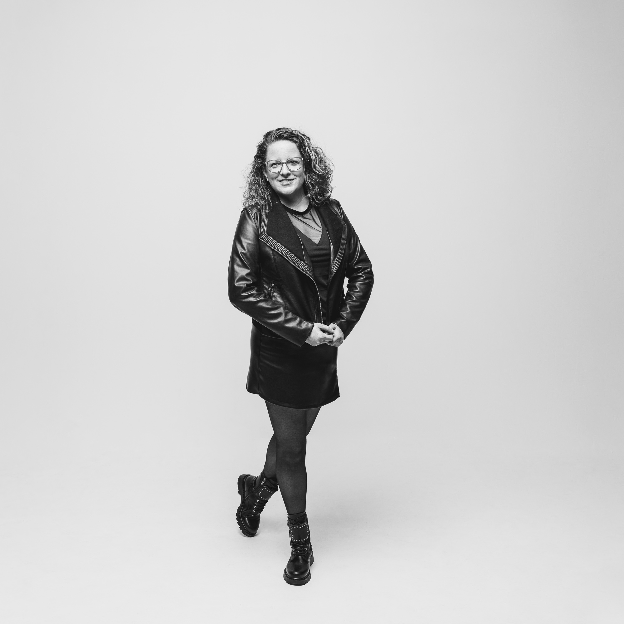 Black and white full-length portrait of a smiling woman with curly hair against a light studio background