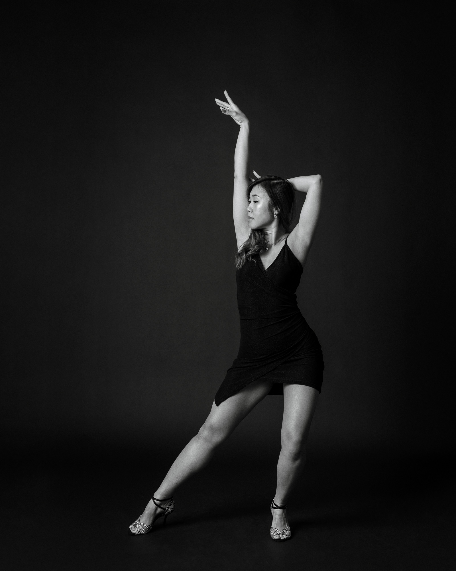 Black and white dance portrait of a woman in an elegant pose against a dark studio background
