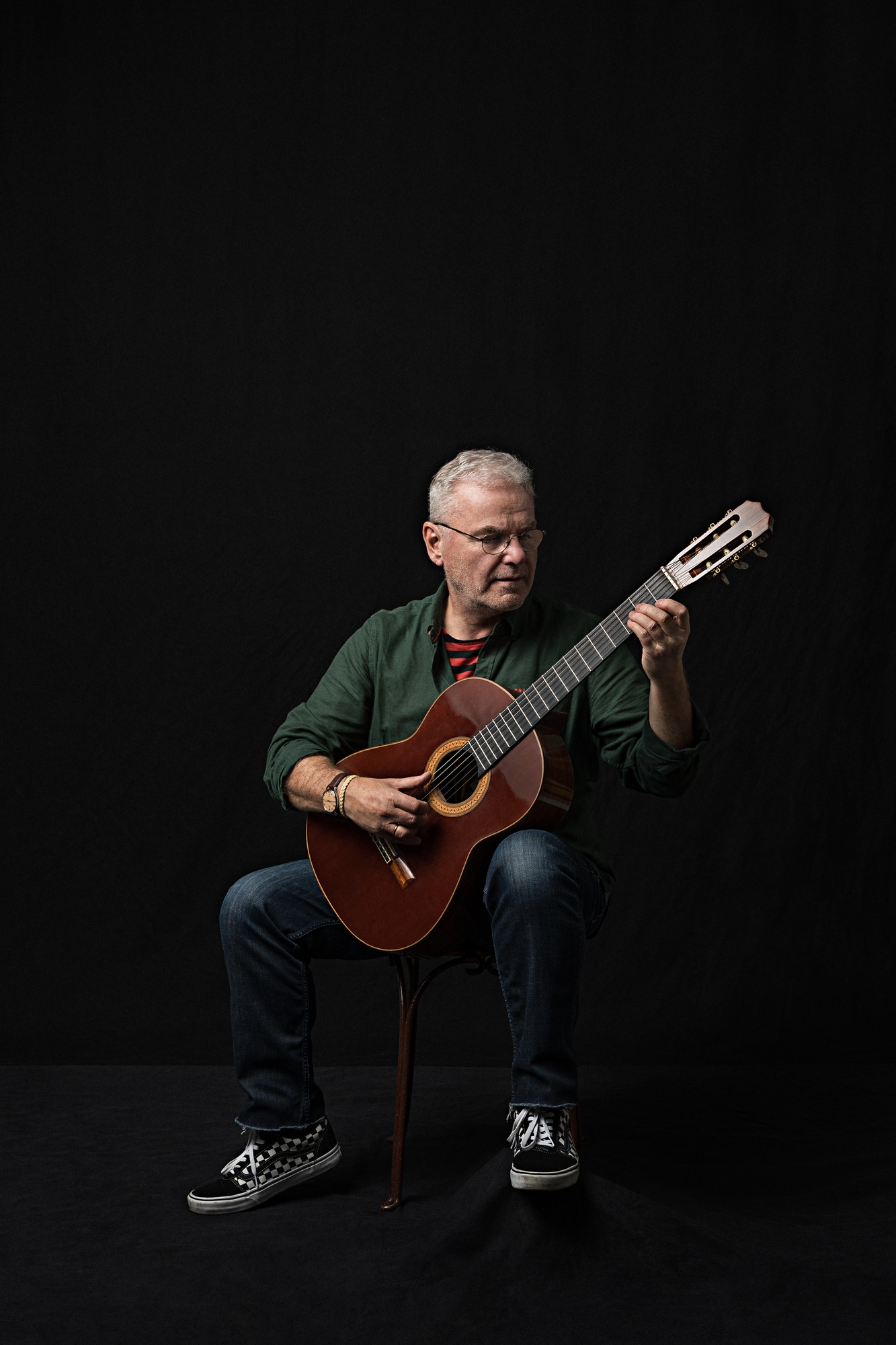 Portrait of a man playing a classical guitar against a black studio background