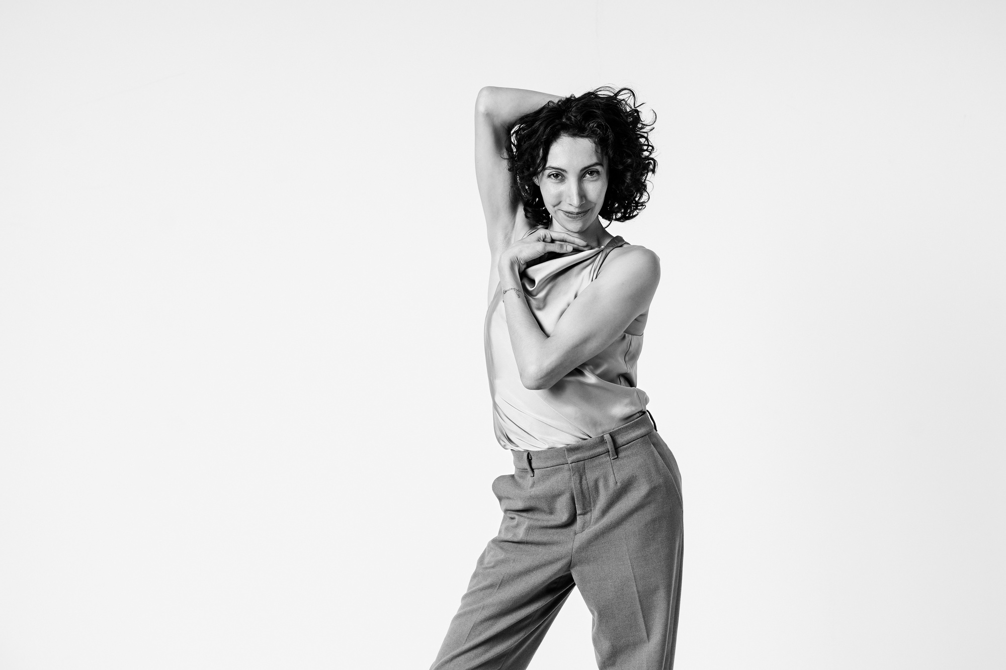 Editorial portrait of a woman with curly hair in an elegant pose against a light studio background